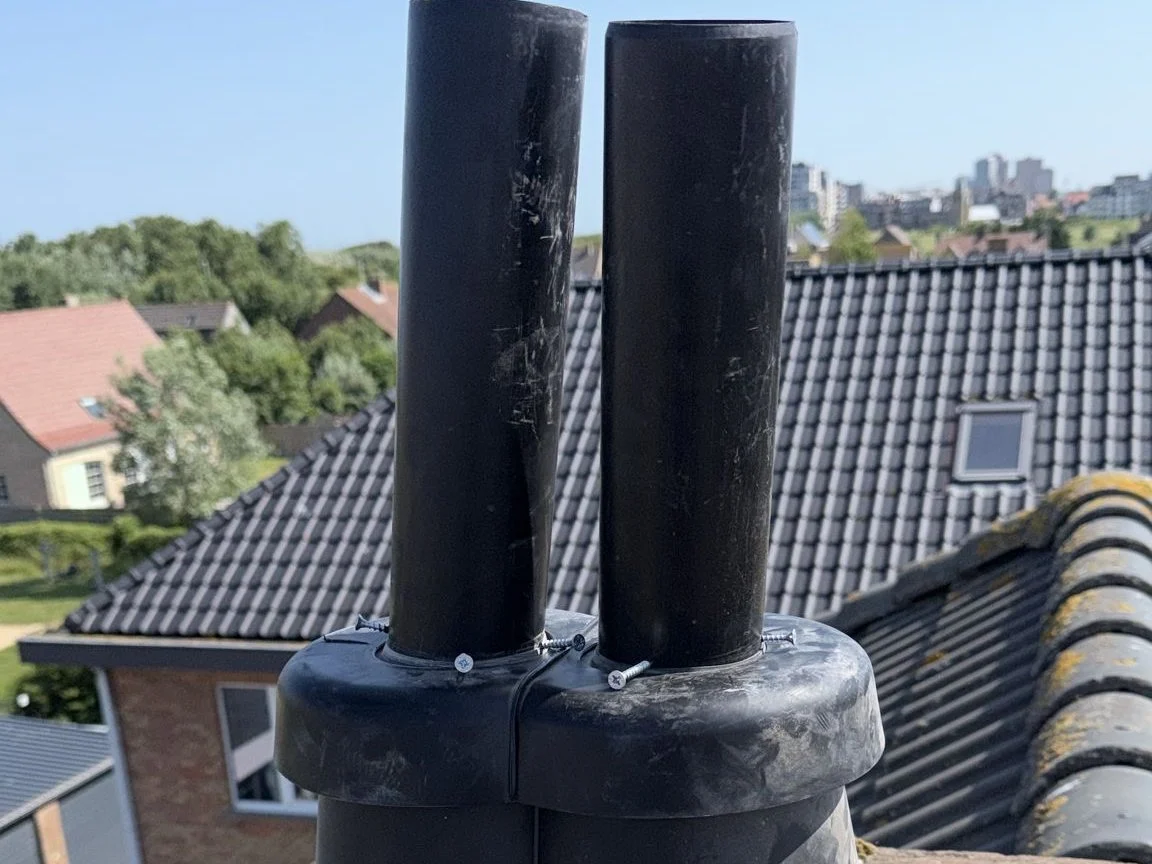 Nieuwe dubbele rookgasafvoer bovenop een schoorsteen, met zicht op de daken