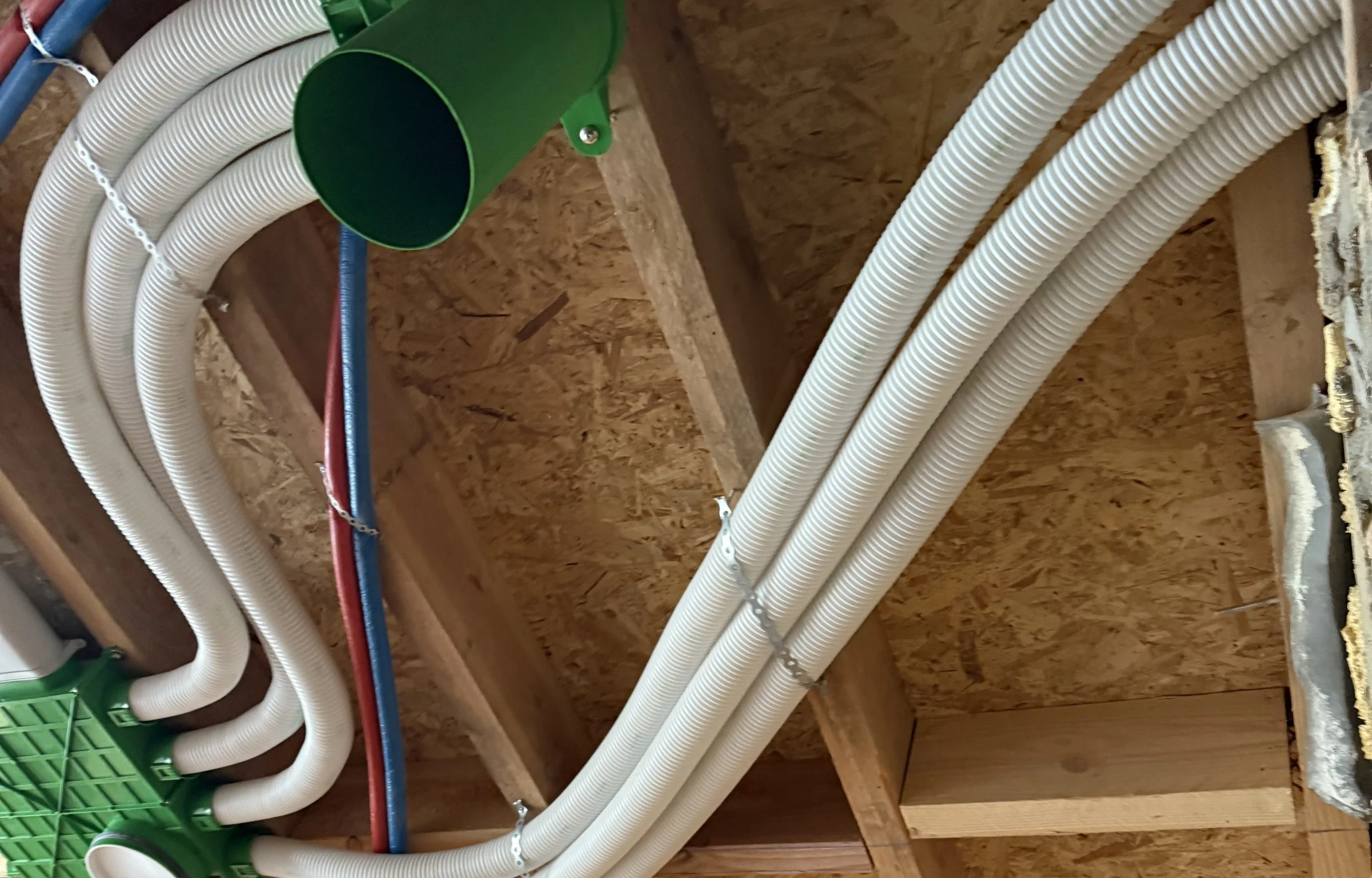Witte ventilatiekanalen die samenkomen in een verdeeldoos in een houten plafond