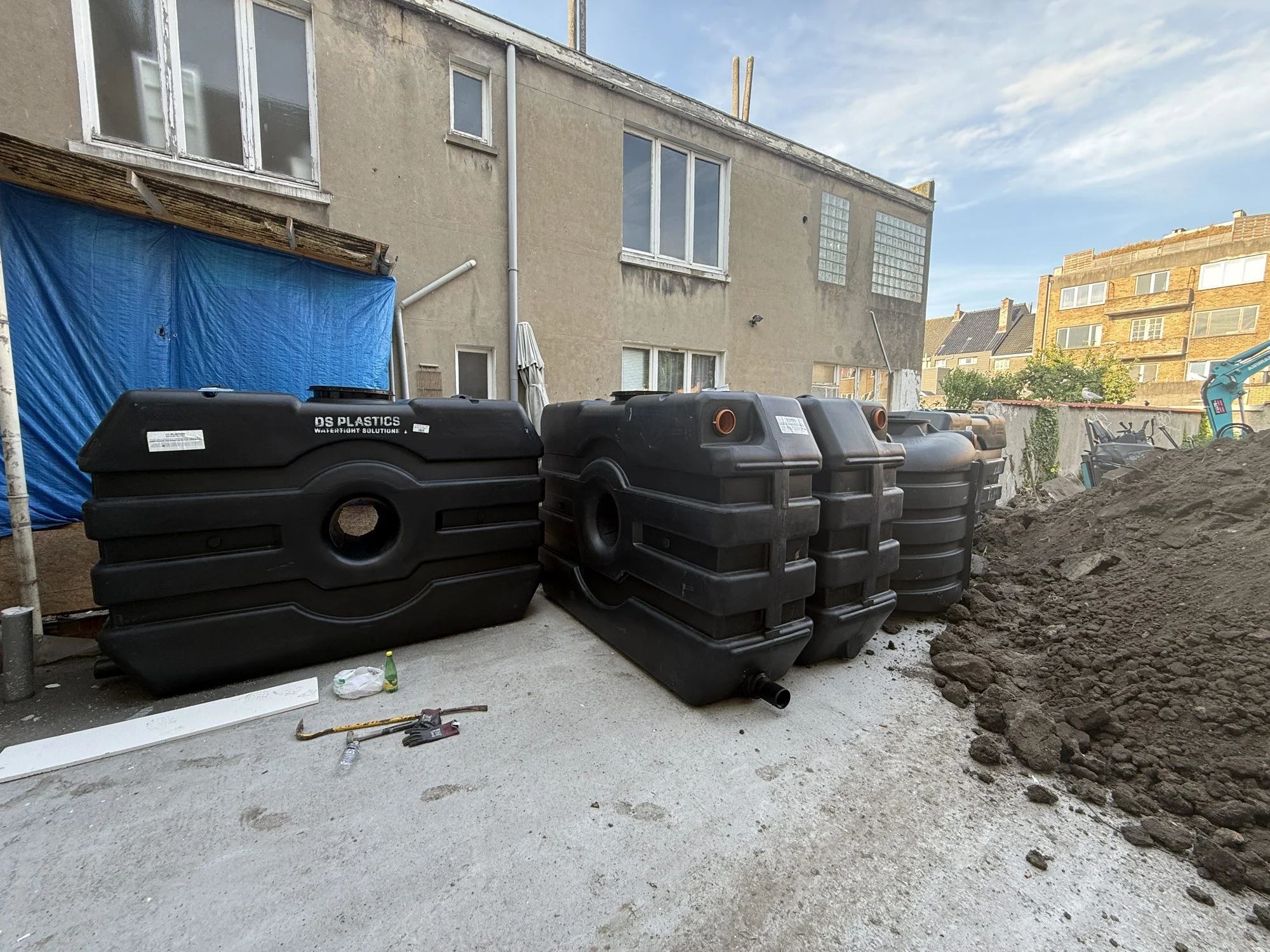Vier zwarte regenwatertanks op een binnenplaats, klaar om ingegraven te worden